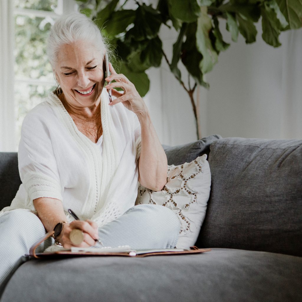 Cheerful elderly woman talking on a phone on a couch