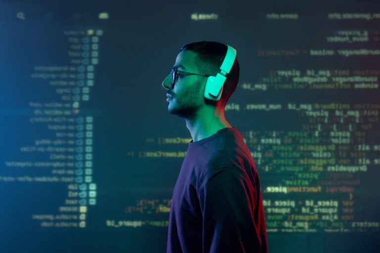 Young programmer in headphones standing against screen with decoded information